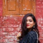 Charming woman in traditional attire posing against a rustic brick wall, showcasing elegance and cultural heritage.